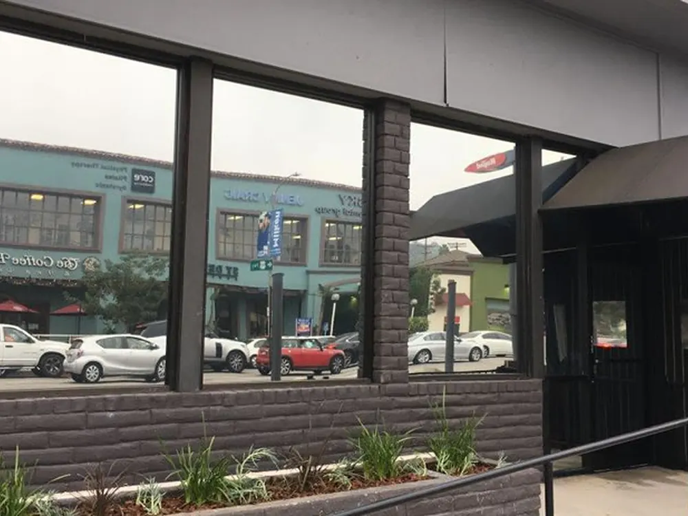 Brick storefront windows with tint film reflecting the shops and parked cars across the street.