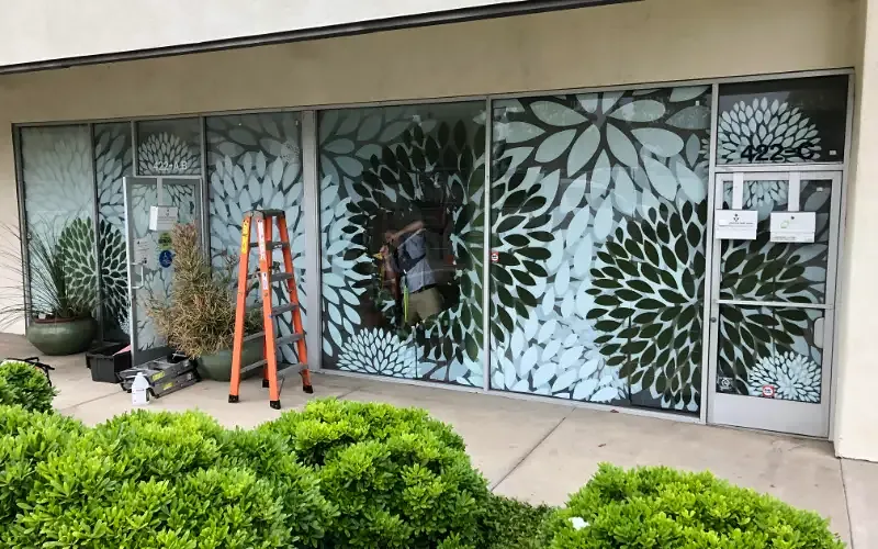 A storefront glazed with a decorative dahlia-pattern privacy film across every pane.