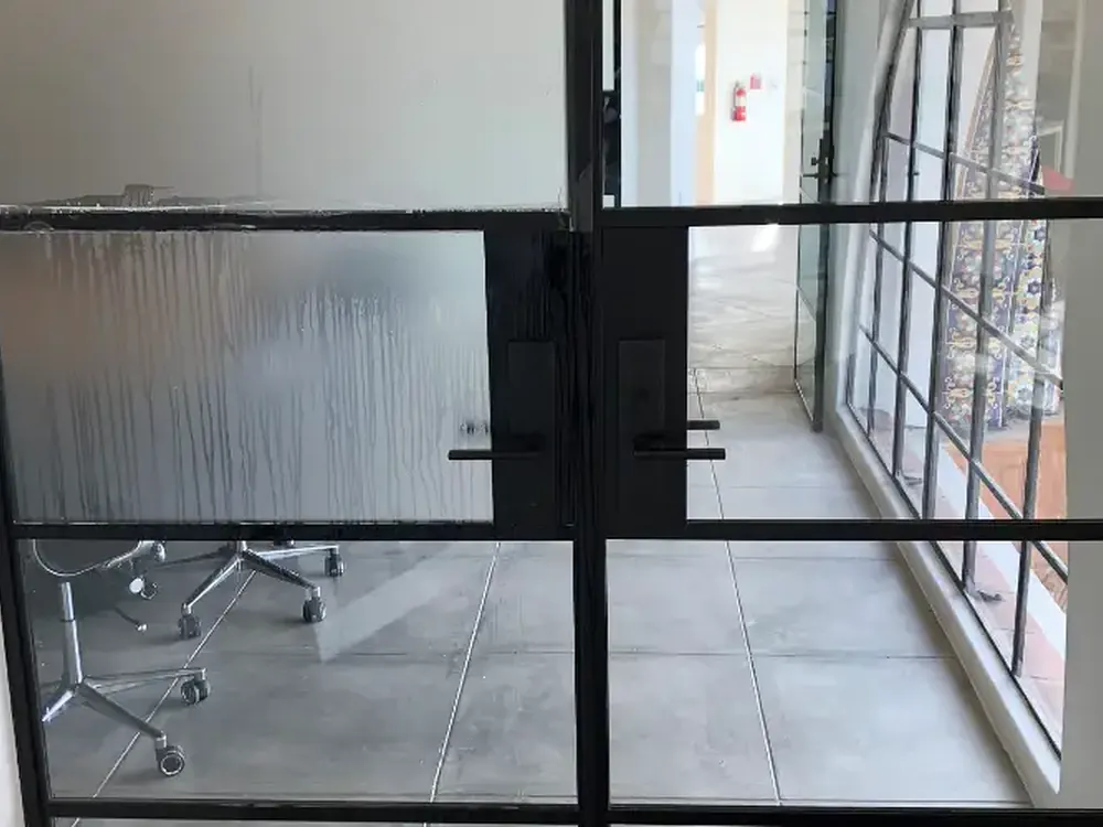 Frosted film being squeegeed onto a steel-framed glass door during installation.