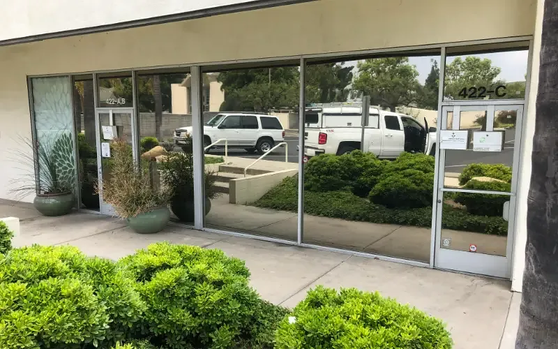 Reflective solar film on a suite of storefront windows, mirroring the parking lot and planting outside.