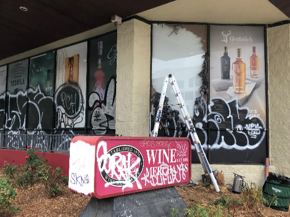 A tagged storefront window wall with the crew and ladder set up to strip and refilm it.